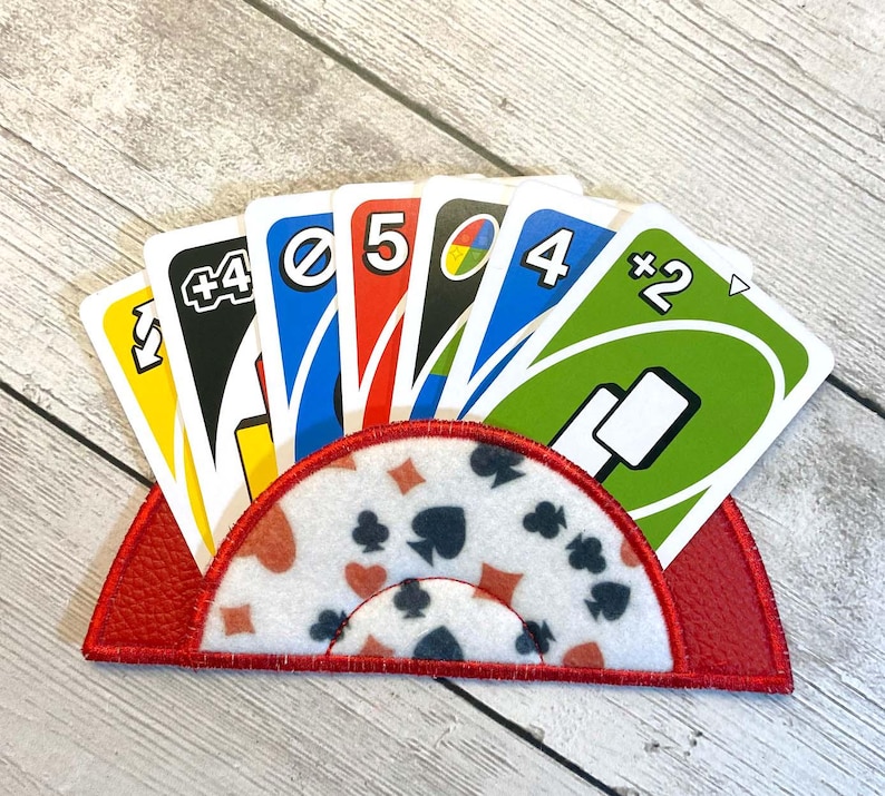May include: A red card holder with a white and red patterned design, holding a hand of Uno cards. The cards are yellow, blue, red, and green, with various numbers and symbols. The holder is made of a textured material.