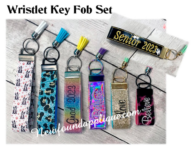 May include: Set of six wristlet key fobs with different designs and colors. The key fobs feature various patterns, including a black and white dog print, a blue and green leopard print, a rainbow glitter design, a gold glitter design, a black and white tie-dye design, and a black and white design with the text "Senior 2023".