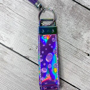 May include: A purple iridescent keychain with a silver key ring and a purple tassel. The keychain has a pattern of white circles on it.