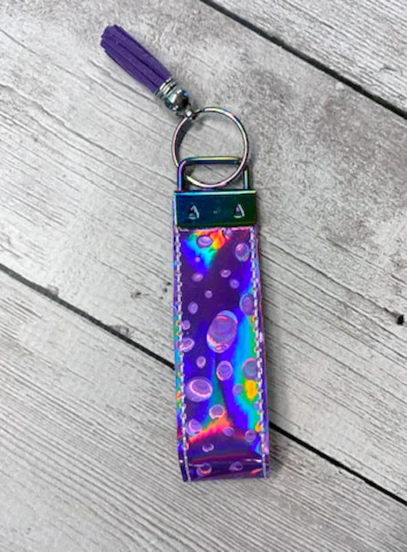 May include: A purple iridescent keychain with a silver key ring and a purple tassel. The keychain has a pattern of white circles on it.