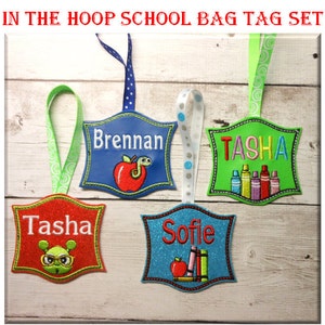 Könnte beinhalten: Ein Set aus vier bestickten Schultaschenanhängern mit Bändern. Die Anhänger tragen die Namen Brennan, Tasha und Sofie und zeigen Motive wie einen Apfel mit Wurm, bunte Buntstifte, eine grüne Figur mit Brille sowie Bücher mit einem Apfel.