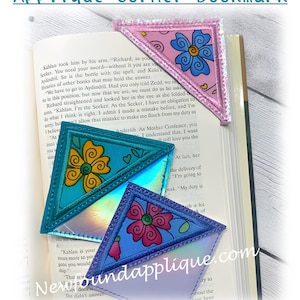 May include: Three corner bookmarks with a floral design. The bookmarks are pink, blue and teal with a holographic finish. The bookmarks are made of fabric and have a stitched edge.