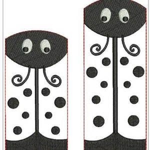 May include: Two embroidered ladybug designs. Each ladybug has a black head with white eyes, a white body with black spots, and a black base. The designs are outlined in red.