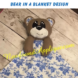 May include: A brown bear applique on a white blanket with a blue floral pattern. The bear has black eyes and a black nose. The text "Newfound Applique.com" is visible in the bottom right corner of the image.