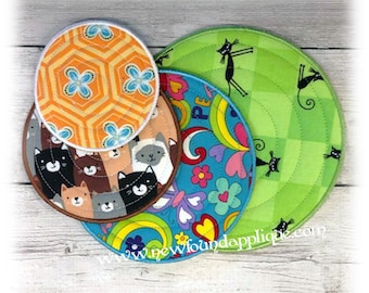 May include: Set of four round quilted coasters with different colorful patterns. One coaster features a geometric pattern in orange and blue, another has a cat and dog pattern, a third has a colorful floral pattern, and the last one has a green and white checkered pattern. The coasters are stacked on top of each other on a wooden surface.