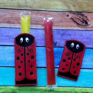 May include: Red ladybug-themed popsicle holders with black accents and a yellow popsicle. A red popsicle is next to the holder. The ladybug design includes black spots and a black head with white eyes.