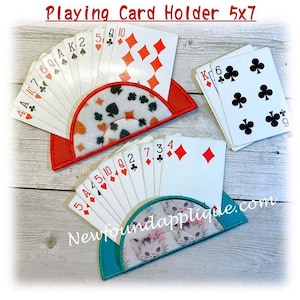 May include: Playing card holders in red and teal, each holding a fan of playing cards. One holder has a pattern of black and orange shapes, the other has a kitten design. The text "Playing Card Holder 5x7" is at the top.