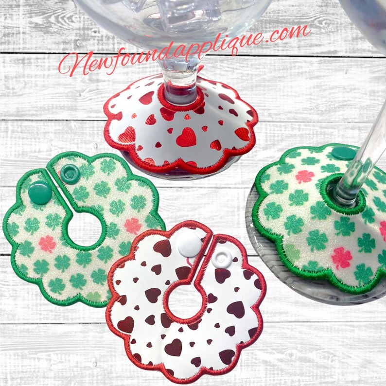 May include: Four decorative wine glass charms. Two charms feature a white background with red hearts and a red scalloped edge. Two charms have a green background with shamrocks and a green scalloped edge. The text "Newfoundapplique.com" is visible.