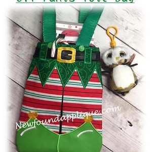May include: Elf Pants Tote Bag with green straps, a red and white striped body, and green elf shoe accents. The bag has a gold buckle and is decorated with green trim. A small owl keychain hangs from the side. The text "Elf Pants Tote Bag" is at the top.