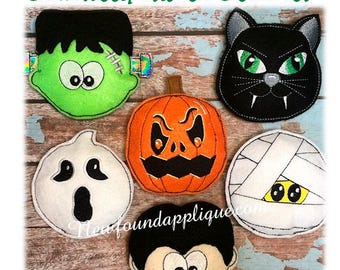 May include: Set of six Halloween-themed felt stuffed heads. The heads include a green Frankenstein, a black cat, an orange pumpkin, a white ghost, a white mummy, and a red vampire.