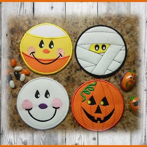 May include: Four round Halloween-themed fabric coasters with embroidered faces. The coasters feature a smiling pumpkin, a mummy, a ghost, and a candy corn.