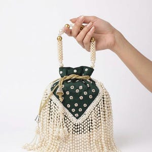 May include: A dark green drawstring pouch bag featuring a white floral pattern, adorned with extensive cream-colored pearl fringe detailing. The bag includes a handle made of cream pearls and gold-tone beads, finished with gold-tone drawstrings.