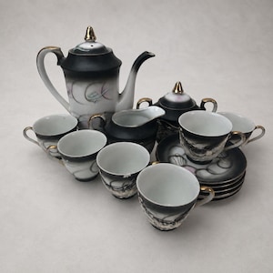 May include: A tea set featuring a teapot, a creamer, a sugar bowl, and several cups and saucers. Each piece is crafted from white ceramic with a black gradient finish, gold-toned accents on the lids and rims, and a swirling abstract pattern.
