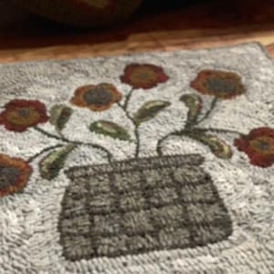 May include: Hand-hooked rug featuring a floral design. The rug has a light gray background with a vase of flowers in shades of brown, red, and green. The vase is a dark gray color.