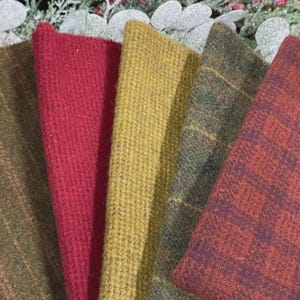 May include: Five folded fabric swatches featuring various textures and patterns. The collection includes a dark olive green with subtle stripes, a solid deep red, a textured mustard yellow, a dark green plaid, and a rust-colored checkered pattern.