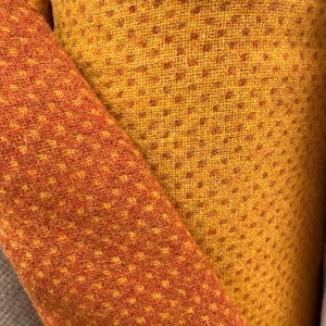 May include: A folded piece of fabric featuring a textured weave with a repeating pattern of small, dark orange dots on a vibrant golden-yellow background. The material displays a consistent, dense, and slightly fuzzy surface texture throughout.