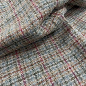 May include: A woven fabric featuring a multi-colored plaid pattern with intersecting lines in shades of light blue, olive green, and vibrant magenta set against a textured, heathered beige and tan background with a soft, fuzzy surface.