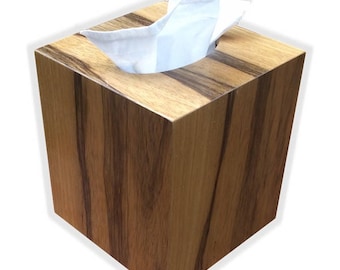May include: A wooden tissue box cover with a natural wood grain finish. The box has a square shape and a slot for tissues.