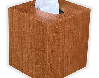 May include: A wooden tissue box cover in a light brown woodgrain finish. The box has a round opening for tissues.