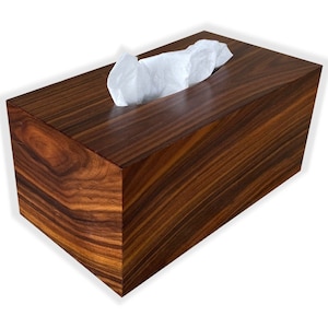 May include: A rectangular tissue box made of dark brown wood with a visible wood grain pattern. White tissues are pulled from a slot on top. The box has a polished finish and a modern design.