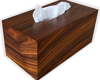 May include: A rectangular tissue box made of dark brown wood with a visible wood grain pattern. White tissues are pulled from a slot on top. The box has a polished finish and a modern design.