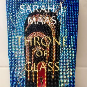 May include: A book cover for "Throne of Glass" by Sarah J. Maas, embellished with iridescent rhinestones. The title and author's name are in white and gold, set against a black and red background. The cover is framed with blue rhinestones.