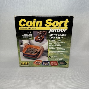 May include: A square cardboard box for Coin Sort Junior coin sorting trays. The black box features yellow text, images of four colour-coded interlocking trays in red, blue, green, and orange, and instructions for sorting pennies, nickels, dimes, and quarters.