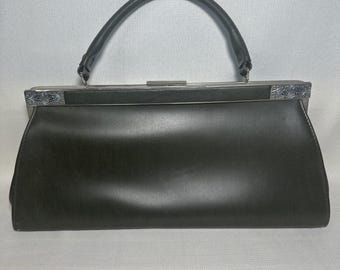 Könnte beinhalten: Eine schwarze Handtasche mit glatter Oberfläche und einem einzelnen, gebogenen Tragegriff. Die Tasche verfügt über einen rechteckigen Metallrahmenverschluss mit silberfarbenen, geprägten Verzierungen an den äußeren Ecken des Rahmens.