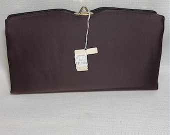 Könnte beinhalten: Eine dunkelbraune, rechteckige Clutch mit glatter, satinartiger Oberfläche und einem goldfarbenen Metallverschluss in der oberen Mitte. Ein weißes Papieretikett ist mit einer Schnur am Verschluss befestigt und trägt den Text GIESCHE 131 120 30075 $1395.