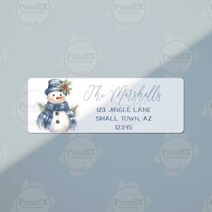 May include: A blue and white snowman with a blue scarf and hat, with a pine branch and berries on his hat. The text "The Marshalls" is written in cursive above the address "123 Jingle Lane, Small Town, AZ 12345".