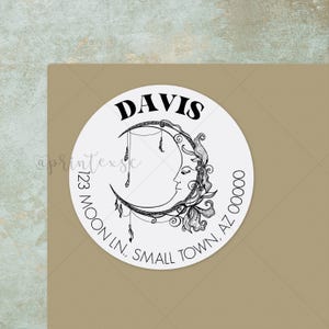 May include: A white round sticker with a black crescent moon design, a face, and floral accents. The word "DAVIS" is at the top. The address is printed around the bottom edge: 123 MOON LN, SMALL TOWN, AZ 00000.