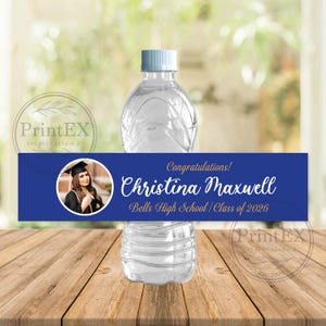May include: A clear plastic water bottle with a blue cap and a custom label. The label is blue with a photo of a graduate, the text "Congratulations! Christina Maxwell, Bells High School / Class of 2026."