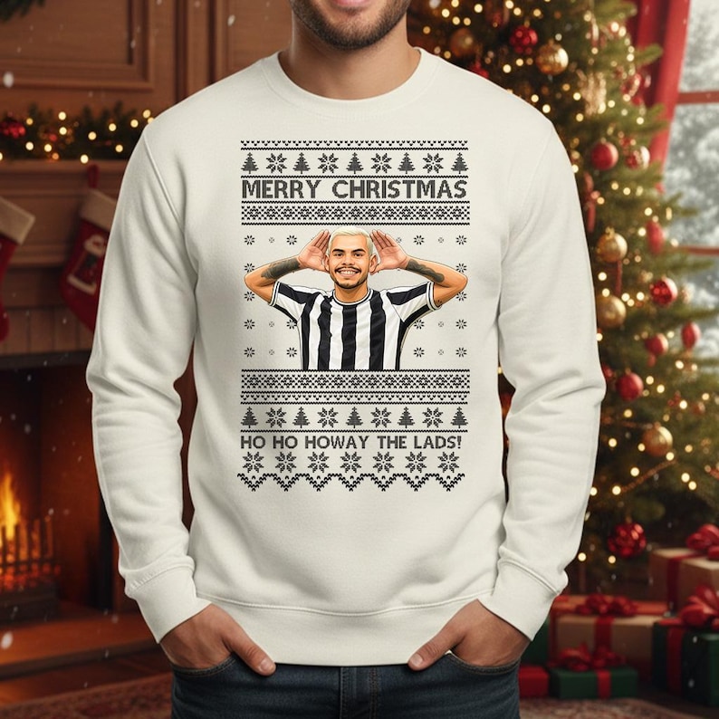 May include: A white Christmas sweater with a festive design. The sweater features the text "MERRY CHRISTMAS" and "HO HO HOWAY THE LADS!". It has a picture of a person wearing a black and white striped shirt.