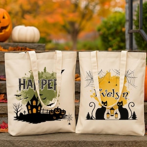 Puede incluir: Dos bolsas de mano crema de Halloween con gráficos y nombres en negro. Una bolsa dice "Harper" con un diseño de casa embrujada. La otra dice "Ivelyn" con siluetas de gatos negros y telarañas. Las calabazas rodean las bolsas.