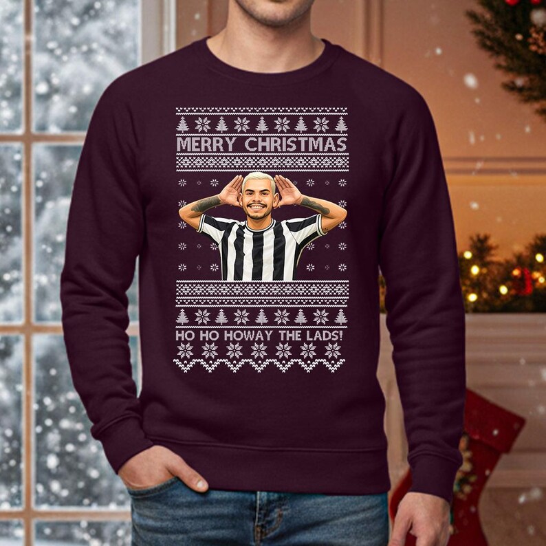 May include: A burgundy Christmas sweater with a festive design. The sweater features the text "MERRY CHRISTMAS" and "HO HO HOWAY THE LADS!" in white. A graphic of a person in a black and white striped shirt is in the center. The sweater has a crew neck.