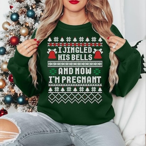 Puede incluir: Una sudadera verde oscuro con un diseño festivo. El texto "I JINGLED HIS BELLS AND NOW I'M PREGNANT" se muestra en blanco. El diseño incluye campanas rojas, copos de nieve y árboles de Navidad. La persona lleva la sudadera.