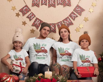 May include: A family wearing matching white t-shirts with a Christmas truck graphic and the text "It's a Atkinson Family Christmas." The scene includes a festive banner, gold stars, and holiday decorations.