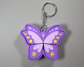May include: A purple butterfly keychain with a silver keyring. The butterfly design features light purple and white wings with yellow accents. The keychain is made of a soft material.