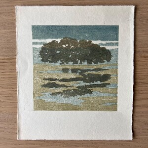 May include: A square print on off-white paper featuring a landscape illustration. The image depicts a dark green tree line against a muted blue sky, with a textured foreground of tan and light blue patches representing a field or water.