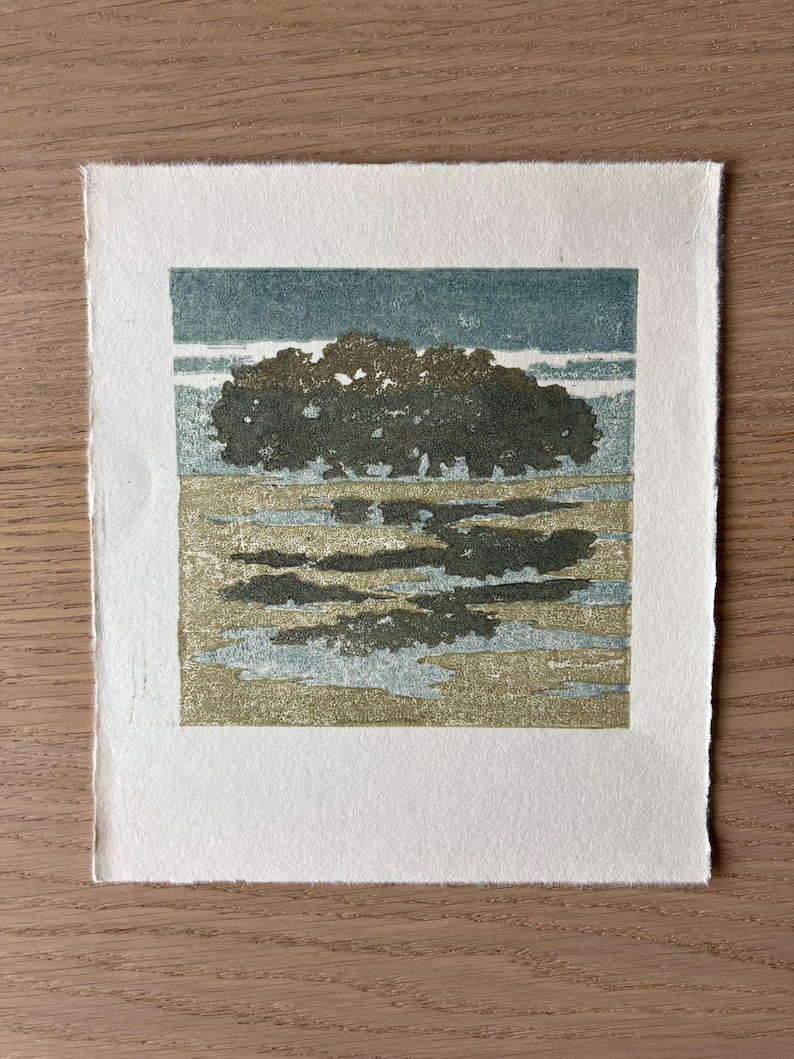 May include: A square print on off-white paper featuring a landscape illustration. The image depicts a dark green tree line against a muted blue sky, with a textured foreground of tan and light blue patches representing a field or water.