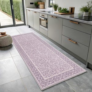 May include: A rectangular, floral-patterned rug in shades of lavender and white, placed on a tiled floor in a kitchen setting. The rug features a detailed border and a central design of stylized flowers and leaves.