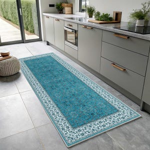 May include: A rectangular runner rug featuring a vibrant teal centre with an intricate floral pattern and a wide white border decorated with detailed dark blue and teal botanical motifs, laid flat on a light grey tiled floor in a kitchen.