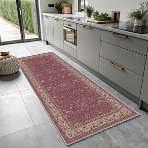 Puede incluir: Una alfombra rectangular tipo pasillo con un centro magenta intenso y un intrincado patrón floral en tonos crema, verde salvia y gris oscuro. La alfombra está enmarcada por un borde ancho y ornamentado en color crema.