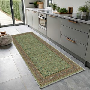 Könnte beinhalten: Ein rechteckiger grüner Teppich mit einem aufwendigen Blumenmuster und einem Rand in Braun- und Rottönen. Der Teppich liegt auf einem gefliesten Boden in einer Küche und verleiht dem Raum eine dekorative Note.