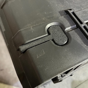 May include: A black, heavy-duty plastic storage case featuring a textured surface and a secure, integrated locking latch mechanism. The case has a rigid, reinforced construction with molded structural ribs and a matte finish on the exterior shell.