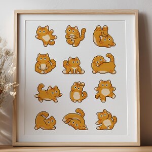 Op de afbeelding: Een ingelijste print met een raster van twaalf illustraties van oranje tijgerkatten in verschillende poses. De katten zijn weergegeven in een pixelachtige kruissteekstijl, tegen een witte achtergrond. De lijst is lichtbruin.