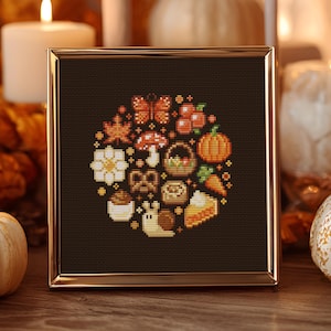 Könnte beinhalten: Ein gerahmtes Kreuzstich-Kunstwerk mit einer kreisförmigen Anordnung von Herbstmotiven. Das Design umfasst einen Kürbis, einen Pilz, einen Schmetterling und andere Herbstmotive in Orange-, Braun- und Weißtönen. Der Rahmen ist goldfarben.