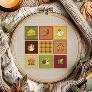 Könnte beinhalten: Ein Kreuzstich-Stickrahmen mit neun Quadraten mit Pixelkunst zum Thema Herbst. Die Quadrate zeigen ein Käse-Stück, eine Eichel, ein Huhn, einen Pilz, ein Karomuster, einen Kürbis, ein Blatt, eine Schnecke und Mais. Die Stickerei befindet sich in einem Holzrahmen.