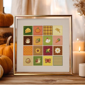 Può includere: Un sampler a punto croce incorniciato con una griglia di quadrati colorati con immagini a tema autunnale. I quadrati raffigurano una zucca, formaggio, ghianda, girasole e altri simboli del raccolto. La cornice è dorata e l'opera d'arte è esposta su una superficie di legno.