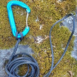 May include: A bright blue metal carabiner with the text STARKNORDIC printed on the side, attached to a long, black braided rope. The carabiner features a silver-colored spring-loaded gate mechanism and is connected to the rope through a loop.